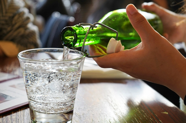 pouring water from green bottle into rocks glass